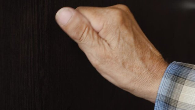 the hand of an old man knocking on the door. Grandfather on the threshold of the house knocking on the wooden entrance door. emotions of old people. lifestyle of pensioners