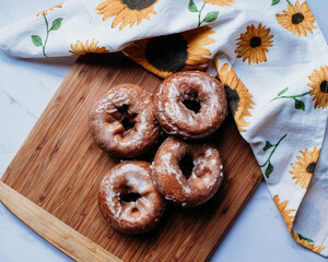 Overhead still-life image of glazed donuts with sunflower towel