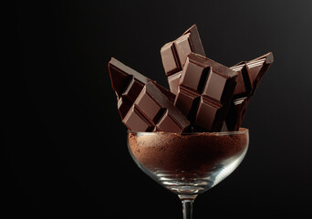Broken black chocolate bar in glass with cocoa powder.