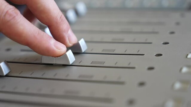professional recording studio sound engineer with finger adjusts volume level mixing console equalizer making music close-up. Hand on a mixer, operating the leader