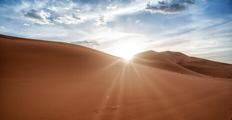 Fototapeta na wymiar Desert dunes landscape with sun flare on cloudy sky background.