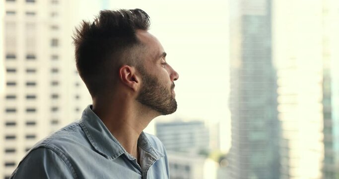Close up portrait of thoughtful Hispanic man looking out window, smiling, enjoy big city view, take deep breath of fresh air, think about new opportunities and bright future, daydreaming feel happy