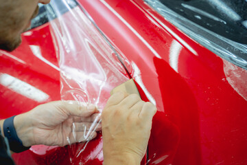 The process of installing protective film on the new red car.