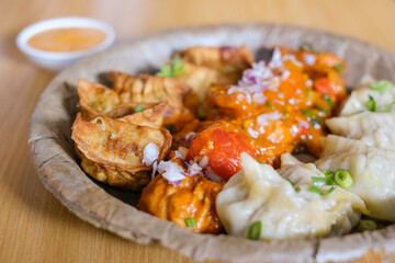 A plate of assorted chicken momos (steamed, fried and chilli sauce dumplings) served on a leaf...