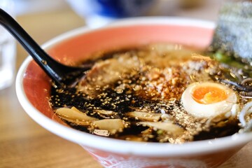 A bowl of tonkotsu ramen with black garlic sauce, chargrilled chashu pieces, bamboo shoots, soft-boiled egg and ladle spoon at Mikazuki, a Japanese restaurant in Sydney