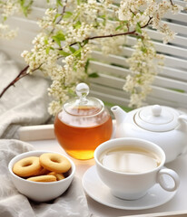 Fototapeta na wymiar White tea set on a wooden table against a background of flowers near the window