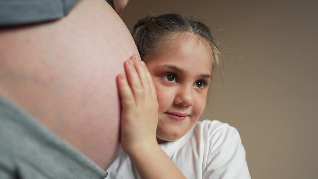 Child girl listening pregnant mother's belly. Little girl listen mother tummy pregnant new baby Happy child holding belly of pregnant woman. Mothers day concept. Maternity, family, parenting concept.