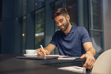 Male manager making notes in notepad during working day in modern office