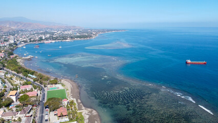 Scenic aerial of coastal capital city of Dili in Timor-Leste with views of blue ocean, coral reef and shipping vessel