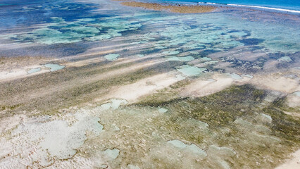 Aerial seascape view of shallow ocean with coral reefs, textured sand patterns and crystal clear water on tropical island