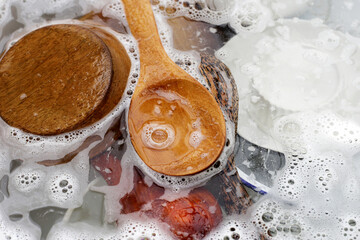 Wooden spoon, cutting board and dishes in water and bubbles of dishwashing liquid