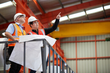 factory workers or engineer planning from work on blueprint drawing paper and pointing to something...