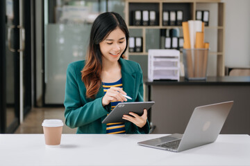 Confident business expert attractive smiling young woman typing laptop ang holding digital tablet on desk in office.