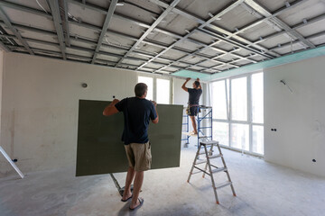 Workers fitting panel into frame of ceiling.