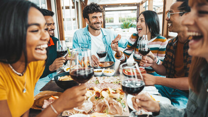 Happy friends drinking red wine sitting at restaurant table - Multiracial young people enjoying rooftop dinner party together - Food and beverage concept with guys and girls having lunch break outside - 658950600