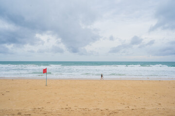 Female tourists walking on the beach with a red flag prohibiting swimming because of strong waves.
