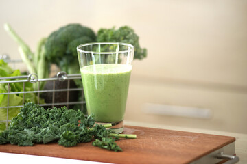 Glass of Kale smoothie with Kale leaves and other green vegetables on food preparation table, healthy drinks concept