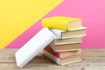 Books stacking. Books on wooden table and pink, yellow background. Back to school. Copy space for ad text.