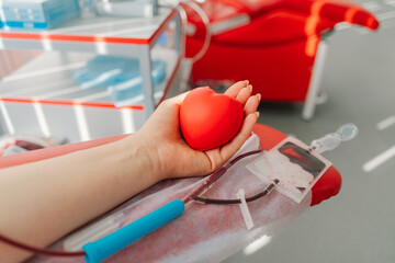Young woman making blood donation in hospital. A woman donates blood while holding a red heart....