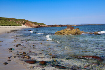 crashing waves on beach with blue water and cliffs in the background