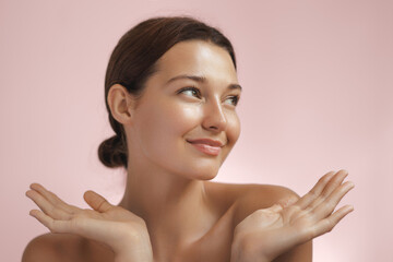 Happy beautiful young adult woman showing her perfect face with healthy shiny skin. Beauty photo of gorgeous girl after morning beauty cosmetic routine finishes daily makeup on pink background. Youth