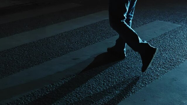 Men's feet walking on a pedestrian crossing in the night city. Slow motion, light from car headlights.