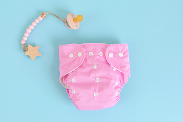 Flat lay with reusable pink cloth baby diaper and pacifier. Eco friendly nappy on blue pastel...