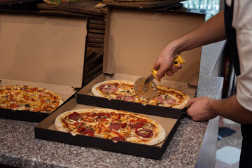 Close up of anonimous pizza chef slicing appetising pizza with cutter wheel in order to be served...
