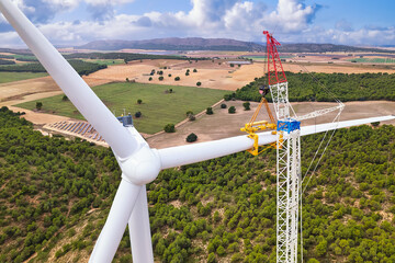 View from above of the installation the rotor blades on a wind turbine with a crane in a windmill farm construction site. Giant crane lifts a rotor blade to the generator. Spain
