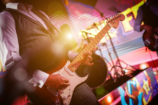 A close-up shot of a guitarist playing their guitar live on stage.