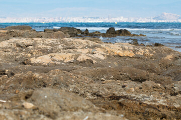Fototapeta na wymiar Playa de piedra en los Arenales del Sol con fondo desenfocado del mar mediterraneo y la ciudad de Alicante, España