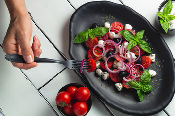 Tomato and mozzarella Caprese salad and pesto sauce with olives on white table served with fork. Food Italian appetizer