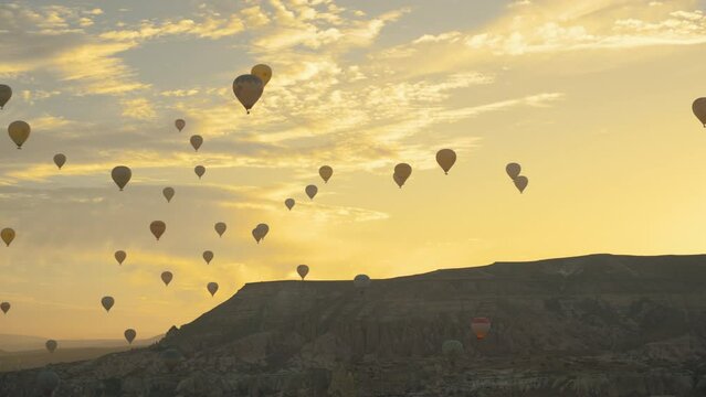 The valley with hot air balloons at sunrise amid the rocks, the sun rising from behind the mountains painted the clouds in golden color, Cappadocia, Turkey.