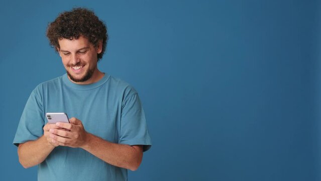 Smiling man holding phone c mockup space in studio on blue background