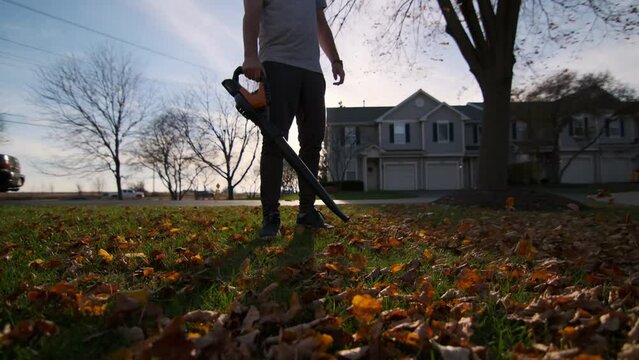 Man blowing leaves in yard in autumn season. Slow motion view