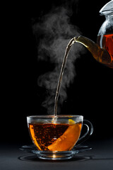 hot black tea pouring from teapot into glass cup with lemon