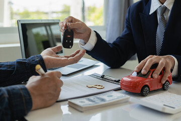 Fototapeta premium Vehicle rental business concept Close up of hands of car rental agent giving car remote key to customer after signing contract on table, sales and insurance concept