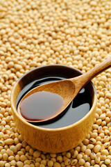 soy sauce in bowl and in spoon on dry soybeans as background