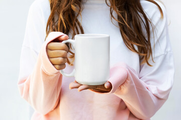 Girl is holding blank 15 oz white porcelain mug in hands and  pink- white sweatshirt . Blank large ceramic cup in hands

