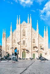 Naklejka na ściany i meble Italy - Milan Duomo cathedral at sunny day - Traveler woman feeds pigeons in the square- Doves flying at Milano Piazza - Travel destinations