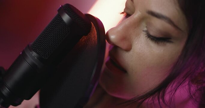 Female music producer in studio with audio recording equipment. Girl singing on a professional studio microphone. Close up abstract video.
