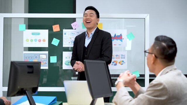 happy asian business man manager giving presentation on glass board speech with coworker conference in meeting room