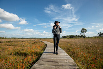 Mid adult woman walking on a wooden boardwalk through marshland, keeping fit and healthy.
