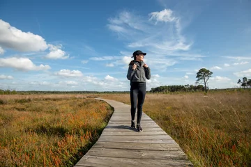 Foto op Aluminium Mid adult woman walking on a wooden boardwalk through marshland, keeping fit and healthy. © Rob Wilkinson