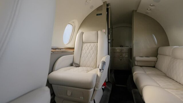Cabin interior of private business aircraft arranged with several beige leather seats and couch. Bright exquisite salon of jet with portholes and ceiling lights