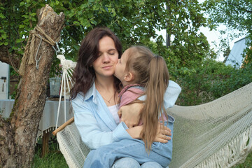 Surrounded by greenery, a mother and daughter cuddle joyfully on a hammock. This moment reflects...