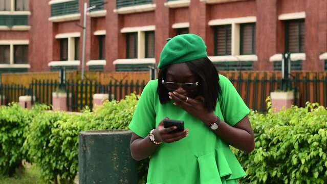 Surprised young black woman happily dancing holding mobile phone