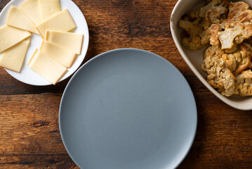 An empty plate on a wooden background stands next to a plate of cheese and deep-fried cauliflower