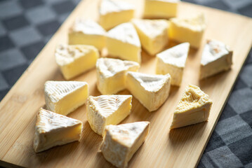Camembert cheese cut into triangles on a wooden cutting board on a dark background
