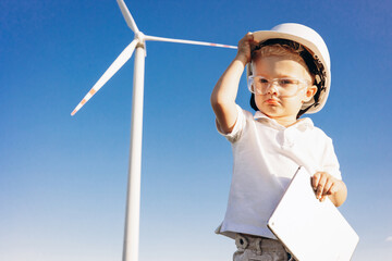 Cute little bou with helmet standing by the windmill turbines